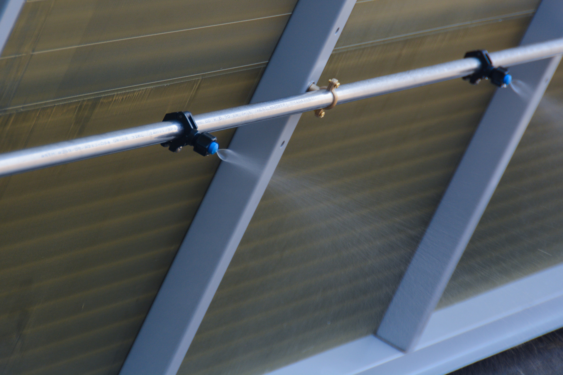 Close-up of adiabatic cooler stainless steel spray bar with atomising nozzles misting water across the coil face